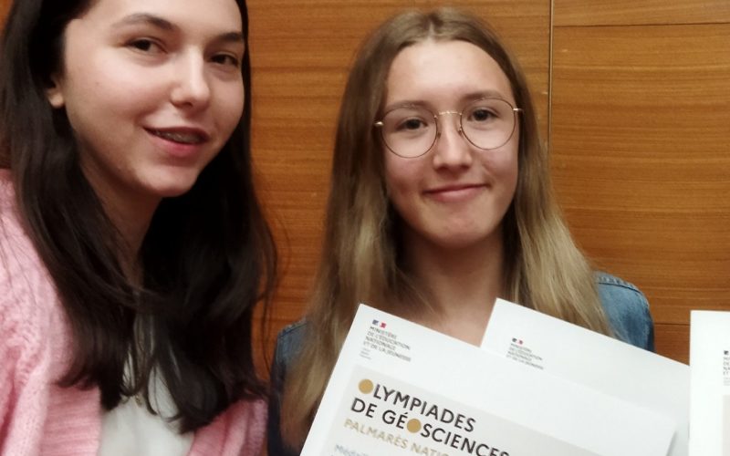 Les élèves Maëline, Anaïs et Léna reçoivent la médaille d'argent lors des Olympiades nationales de géosciences à Paris, accompagnées de leur professeur, Mme Lucie Loyer, devant une exposition de minéraux à Sorbonne Université.