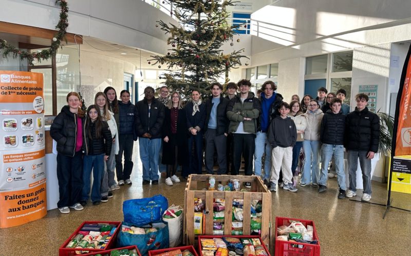 Elèves et adultes du collège souriants et enthousiastes, entourant les boîtes de dons remplies de denrées alimentaires et de produits d’hygiène, symbolisant leur engagement dans la collecte de Noël pour la Banque Alimentaire.